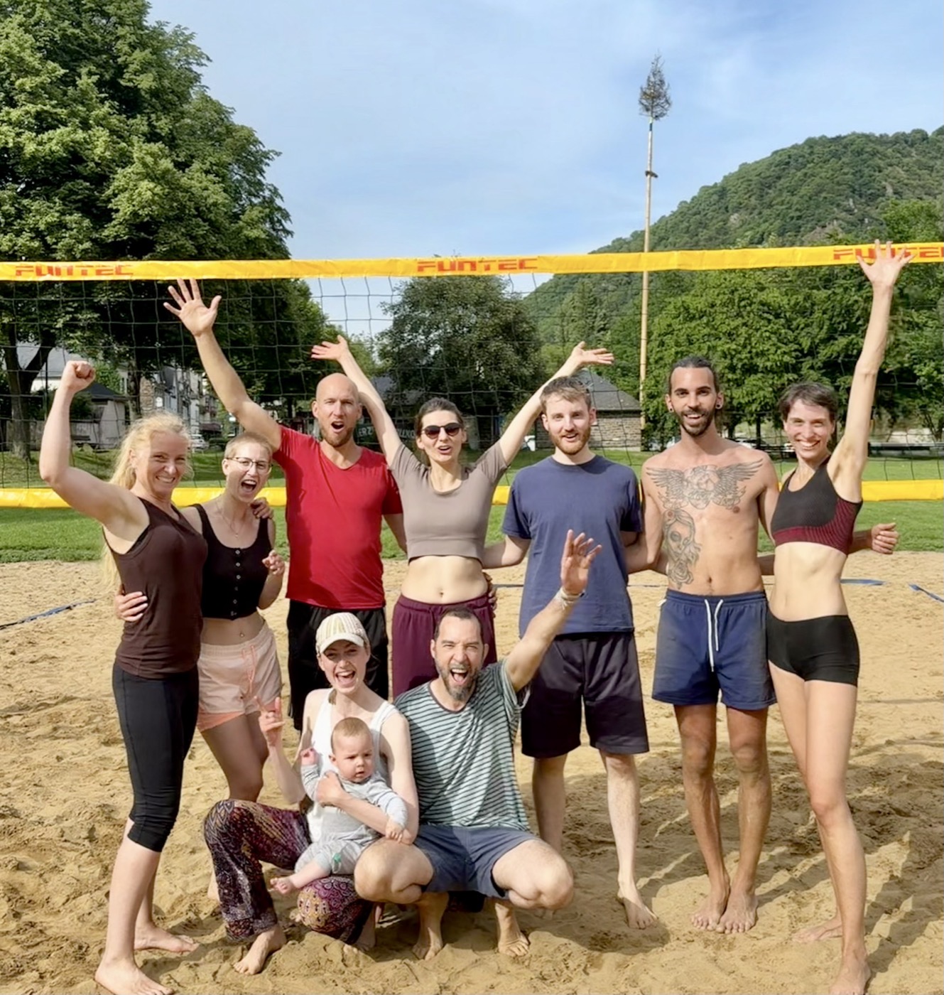 Gruppenfoto der Gemeinschaft nach einem Volleyballspiel im Sand, alle mit erhobenen Armen